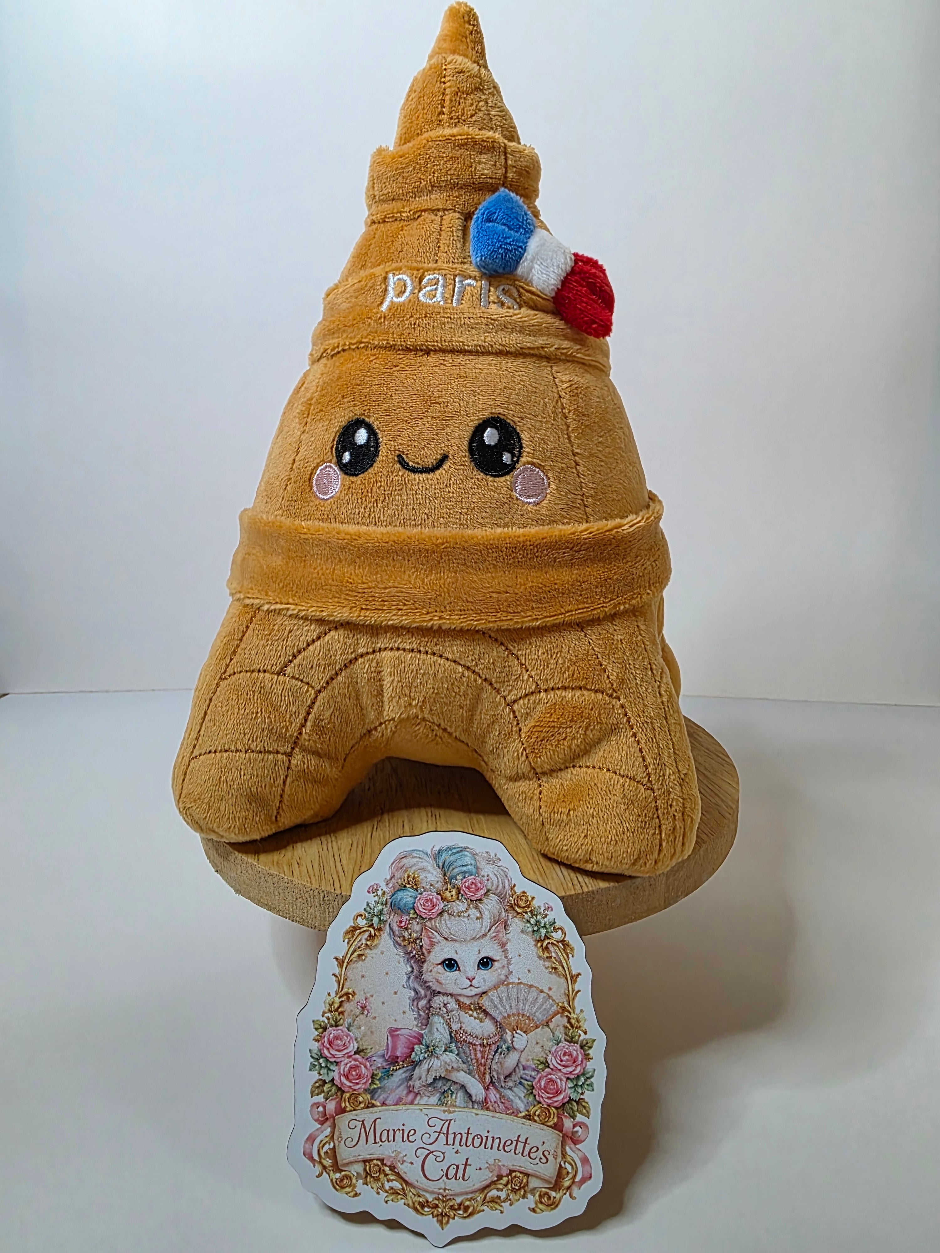 A plush toy shaped like the Eiffel Tower with a cute face and the word Paris and a French flag.